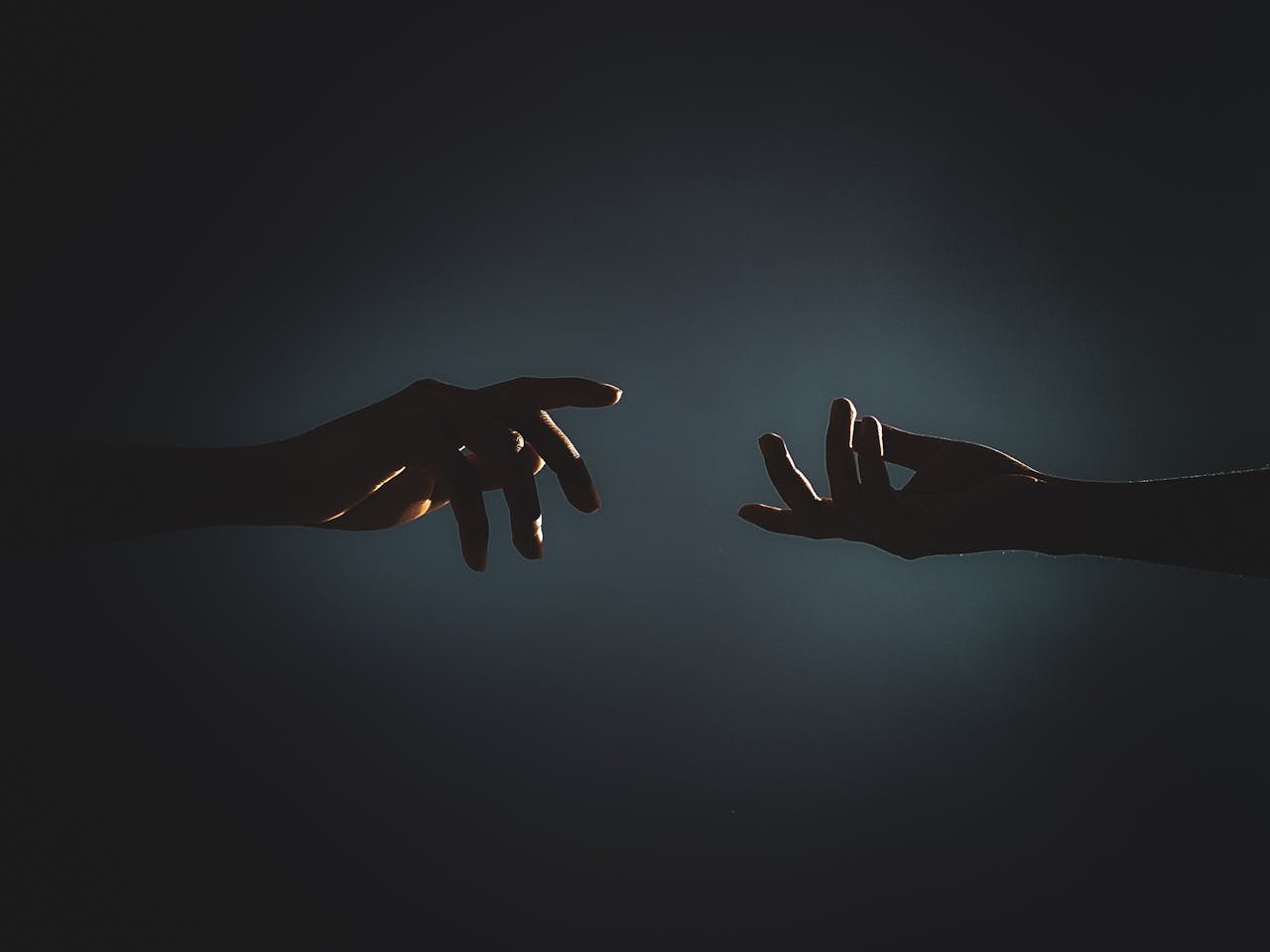 heros-img Dramatic silhouette of hands reaching towards each other in a dark setting, symbolizing connection.